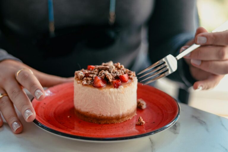 Close-up of creamy cheesecake topped with strawberries and walnuts on a red plate.