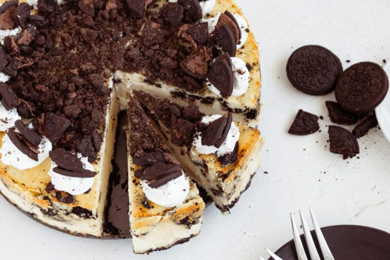 A close-up of a creamy Oreo cheesecake topped with cookie crumbles and whipped cream.