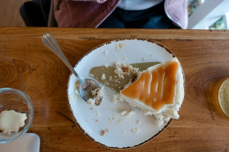 Um Prato Branco Coberto Com Um Pedaco De Bolo Ao Lado De Uma Colher NT_sUGIPH5I