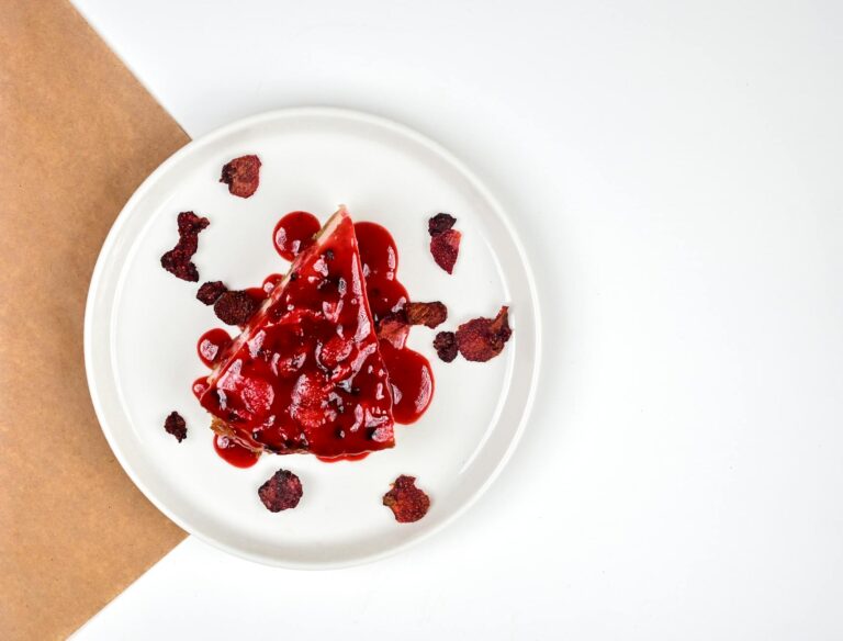 A tempting slice of berry cheesecake with red glaze on a minimalist white plate.
