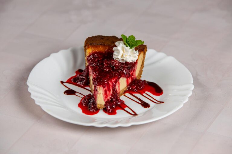 A close-up of a raspberry cheesecake slice with raspberry sauce and mint garnish.