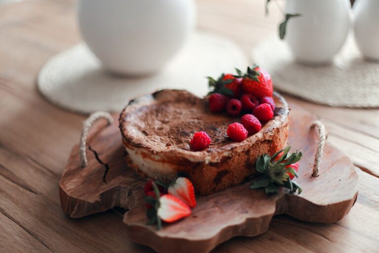 Delicious homemade cheesecake topped with strawberries and raspberries on a rustic wooden serving board.