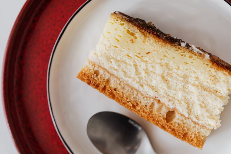 Closeup of yummy piece of cake with chocolate cream served on white plate with tea spoon placed on red plate
