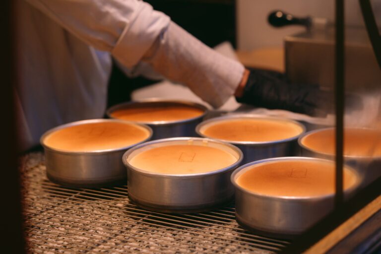 A baker carefully prepares cheesecakes in a kitchen using round pans.