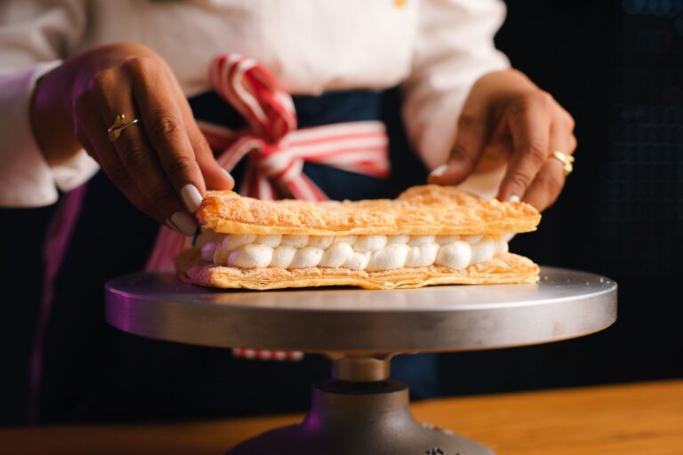 Close-up of a pastry chef assembling a delicate mille-feuille dessert with precision and care.