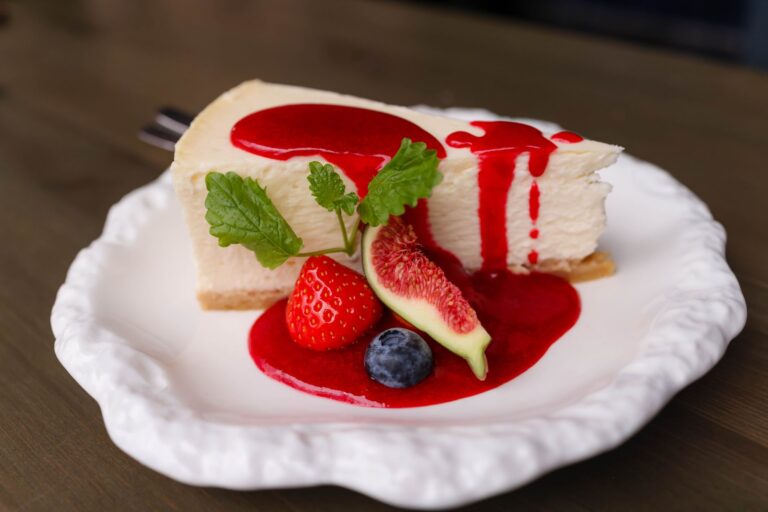 Creamy cheesecake with berries and fig on a white plate. Topped with red fruit sauce.