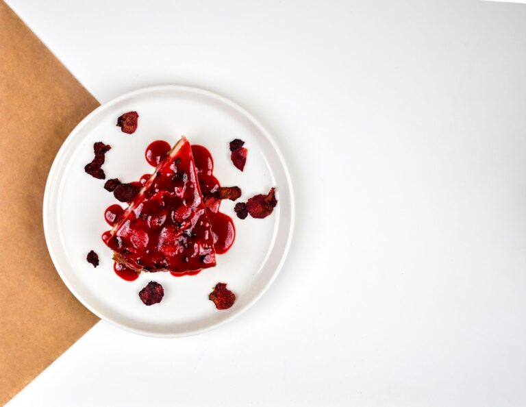 Top view of a raspberry cheesecake slice with sauce and raspberries on a white plate.