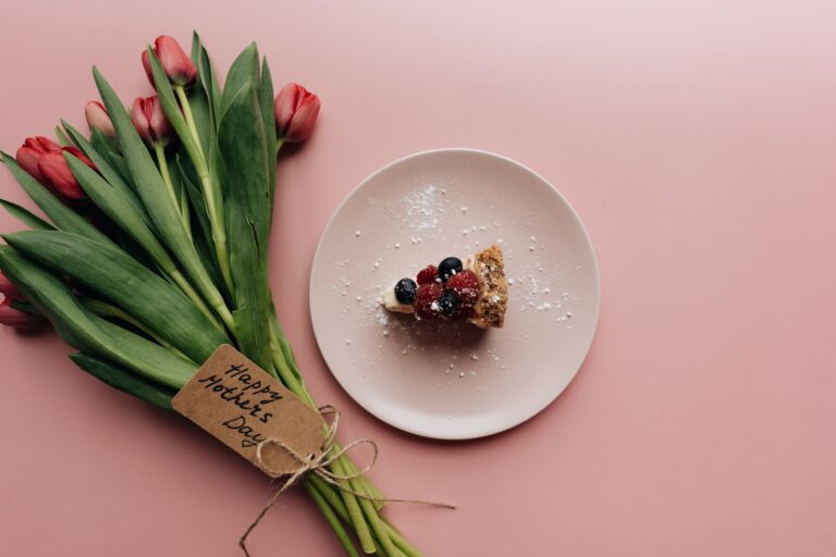 Pink background with a slice of berry cheesecake and a bouquet of tulips for Mother's Day.