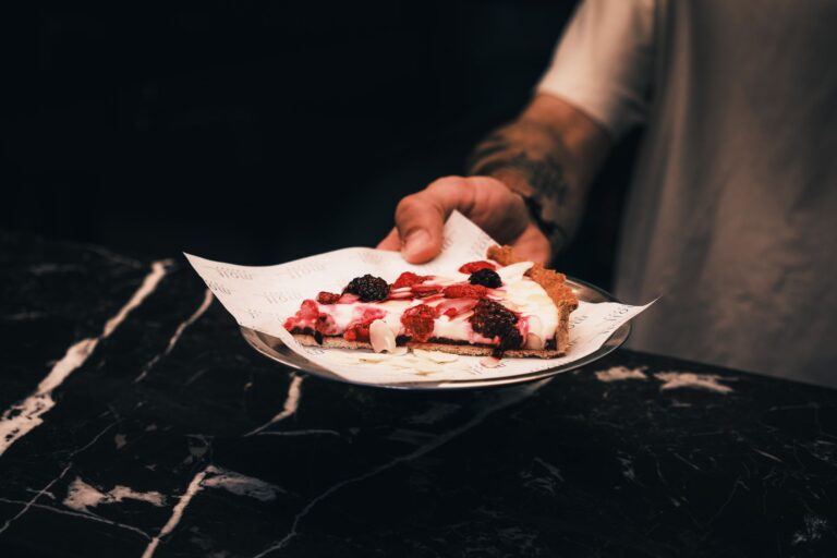 Close-up of a delicious berry dessert tart served by hand on a stylish dark background.