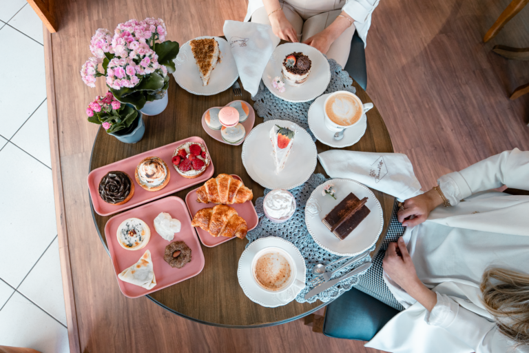 Top view of beautifully arranged desserts and coffee on a cafe table with two people.